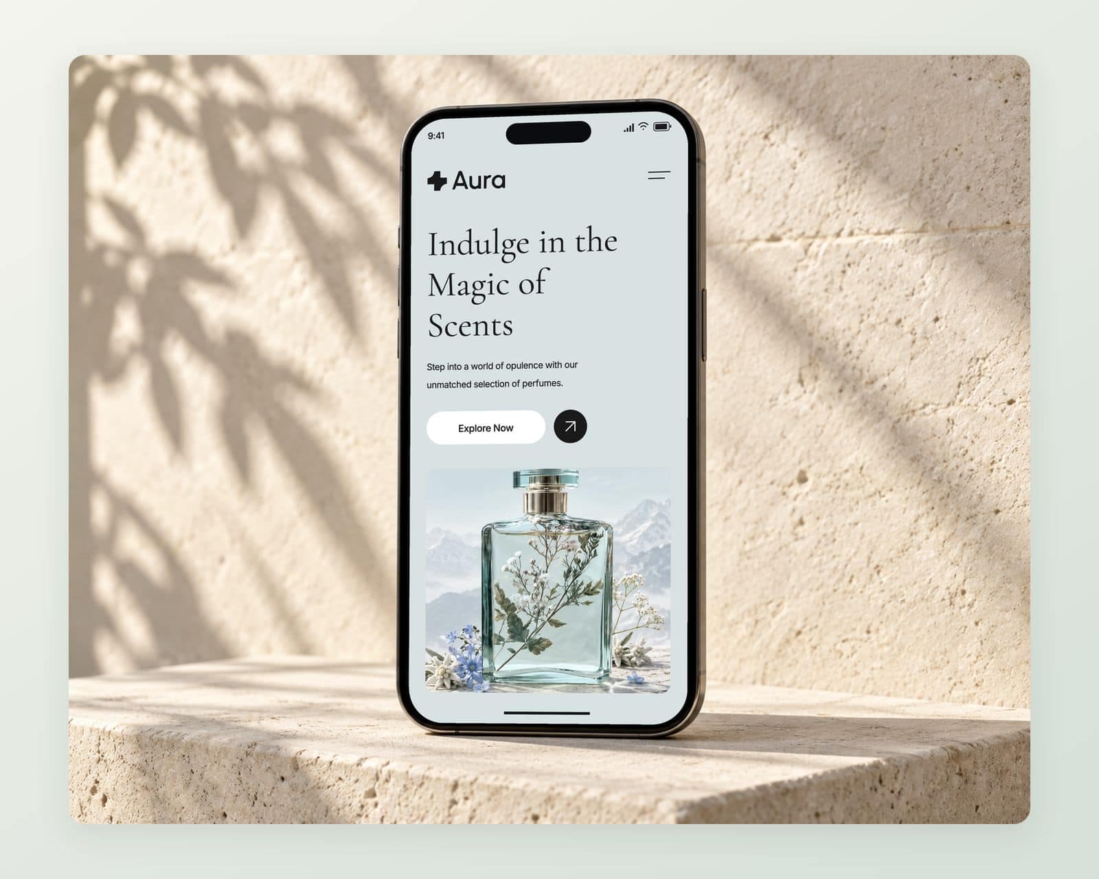 Aura’s homepage on a phone with the serif headline Indulge in the Magic of Scents, the Explore Now button and the Alpine Mist bottle on a pale aqua landscape