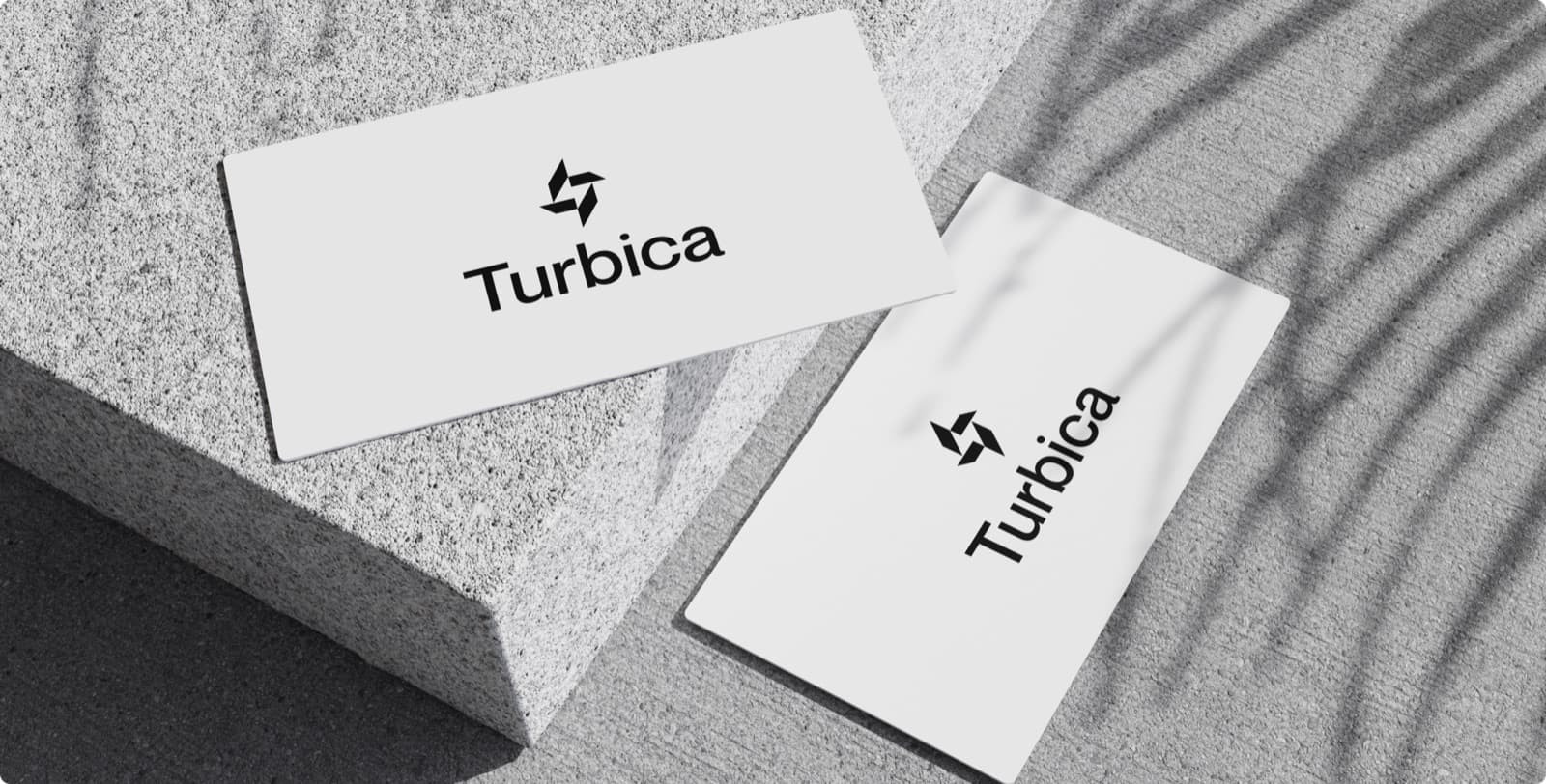 Two white business cards with the Turbica mark and wordmark, lying on grey stone