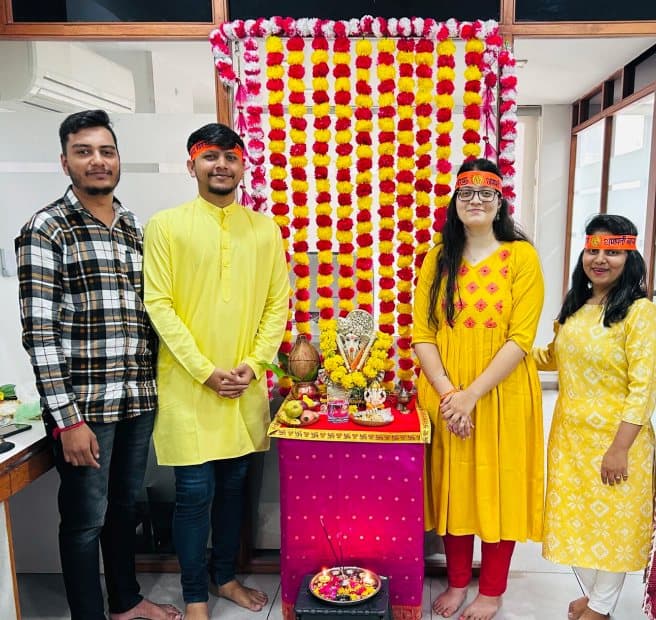 Team members in festive clothes beside a decorated Ganesh shrine in the office