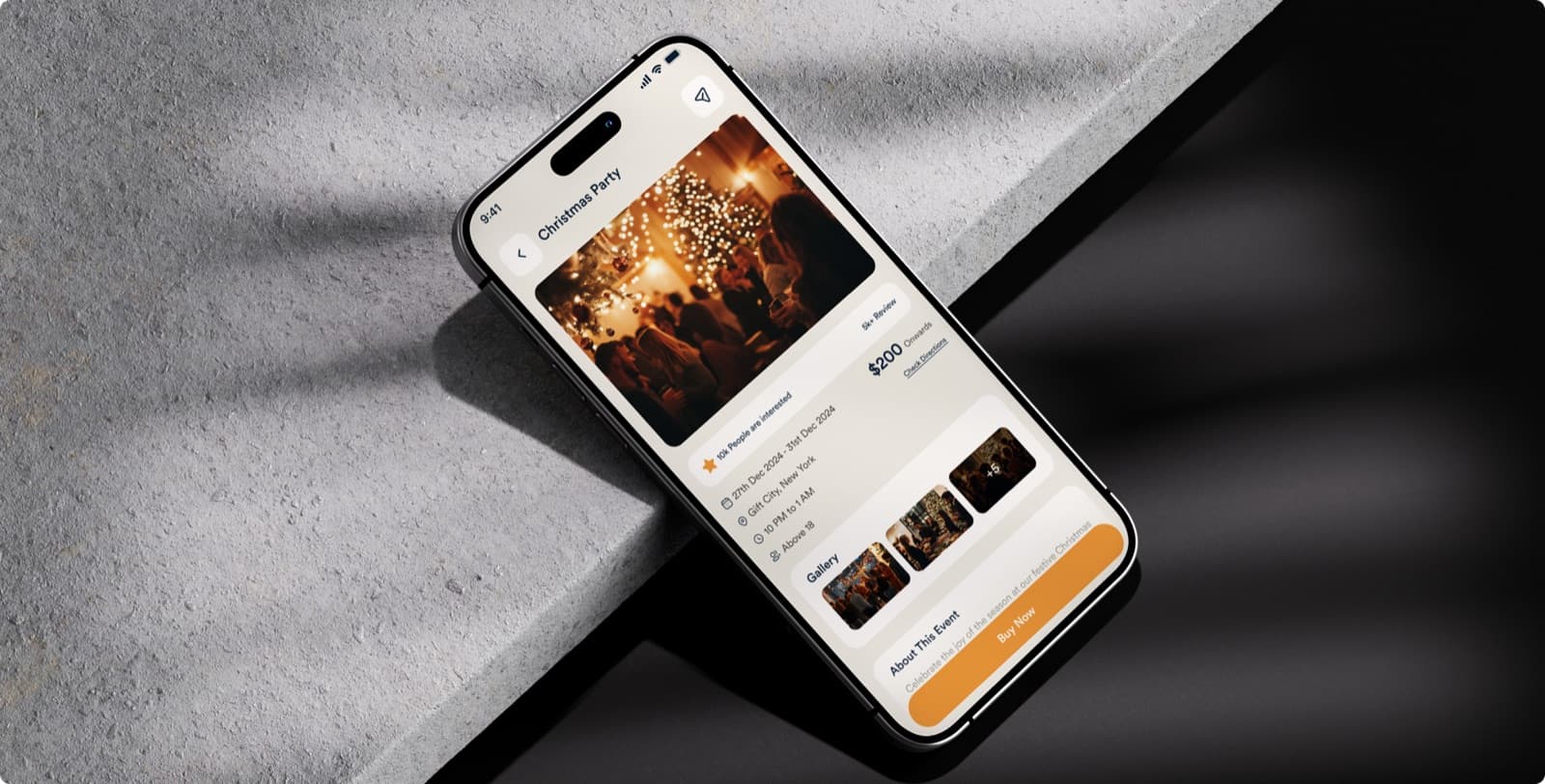 The Nexvent app on a phone lying on concrete, showing the event page for a Christmas party with its dates, a photo gallery and a Buy Now button