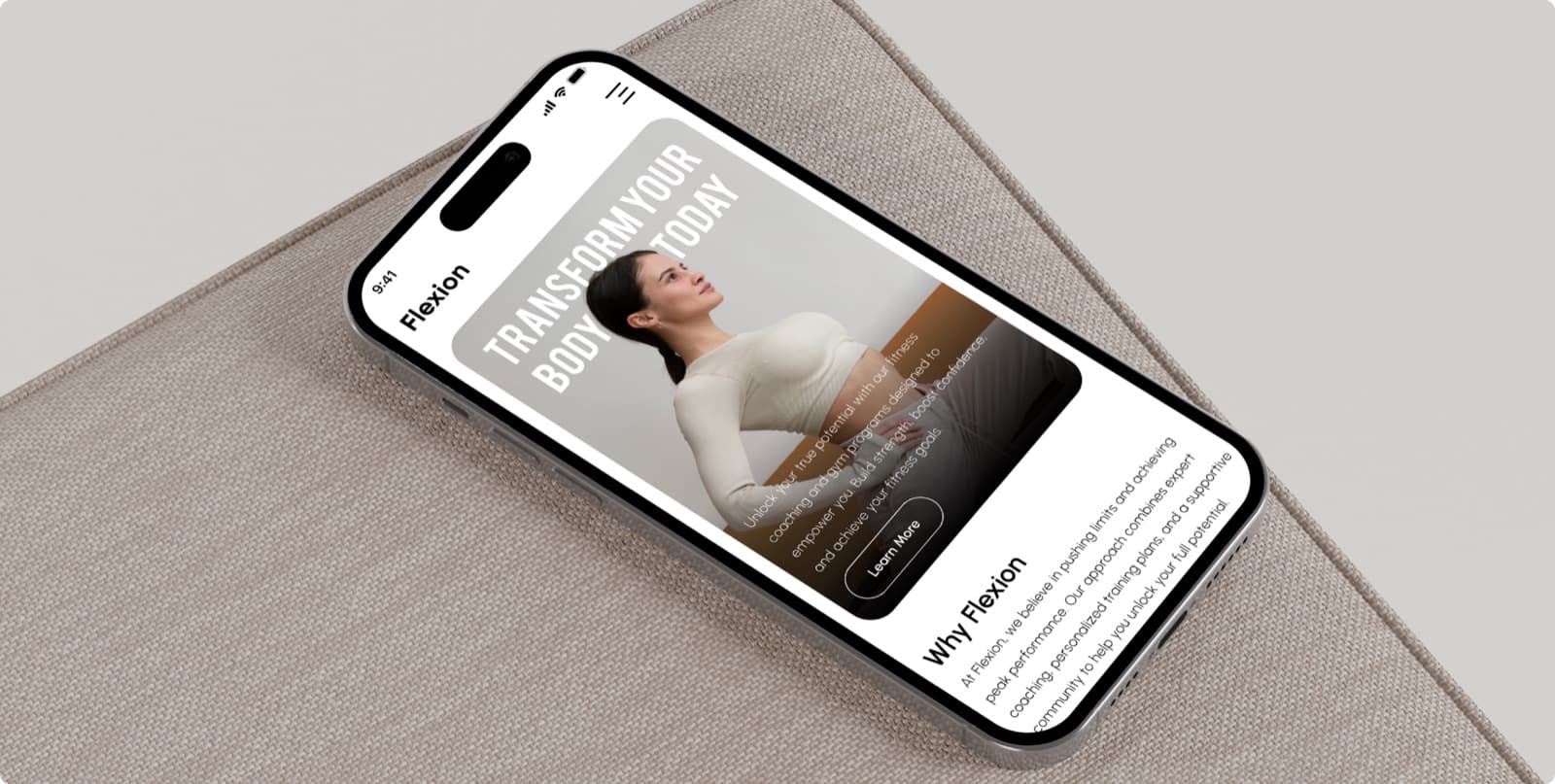 The Flexion homepage on a phone lying on a fabric cushion, with the headline Transform Your Body Today