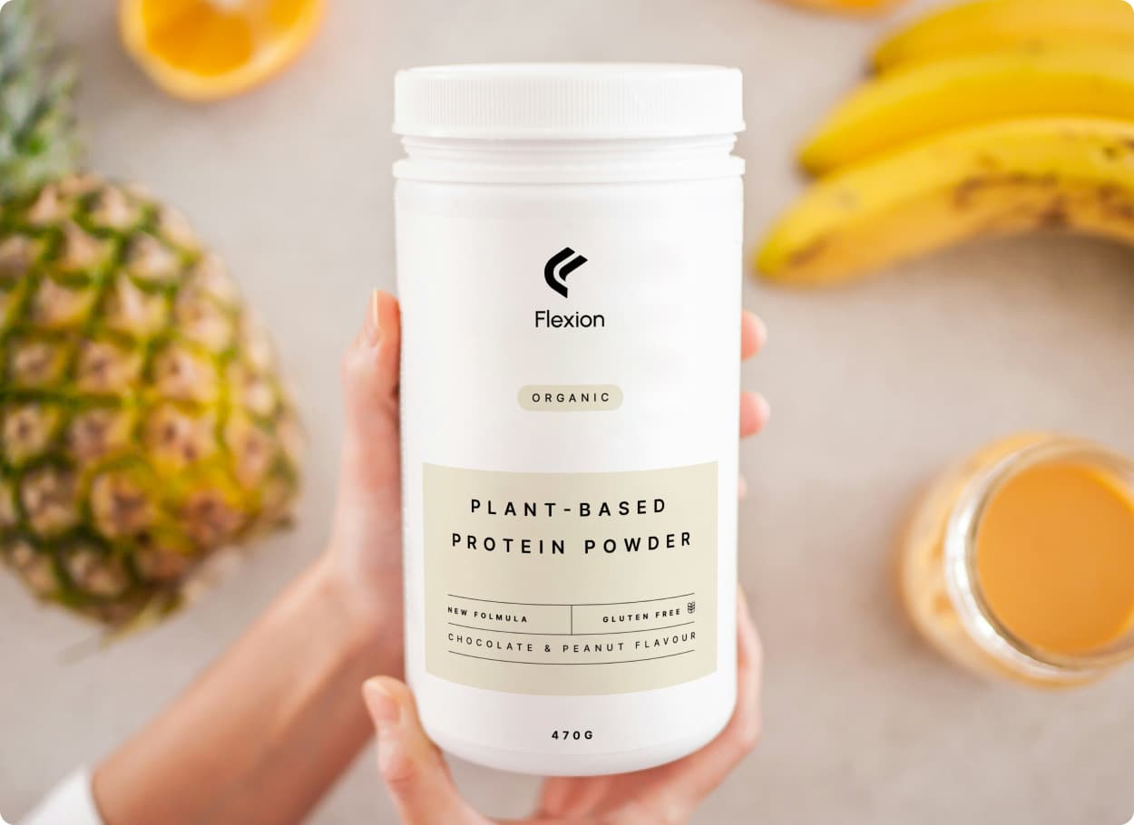 A hand holding a white tub of plant-based protein powder that carries the Flexion mark