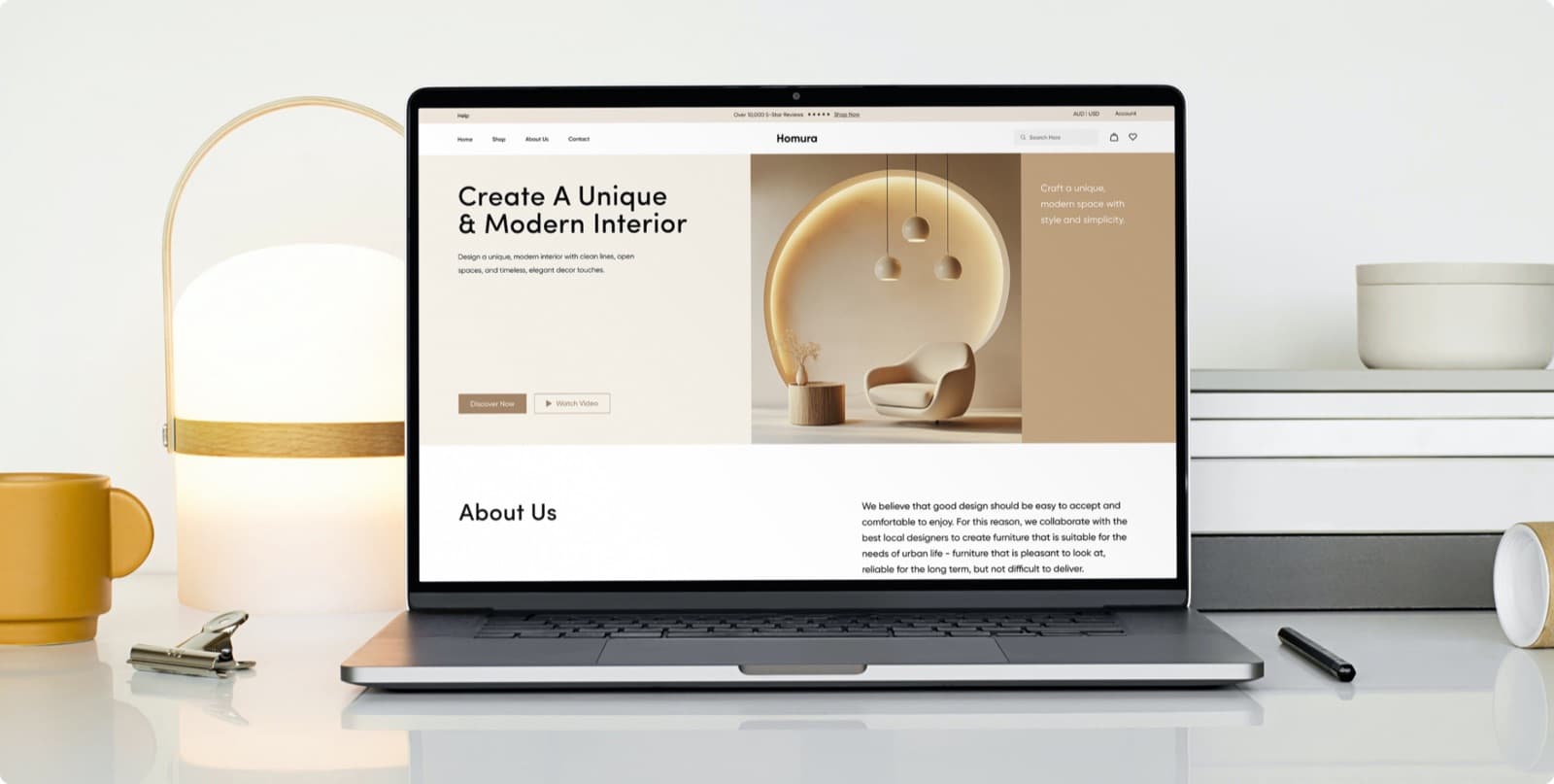 The Homura website on a laptop on a white desk, with the headline Create A Unique & Modern Interior beside a picture of an armchair under pendant lights