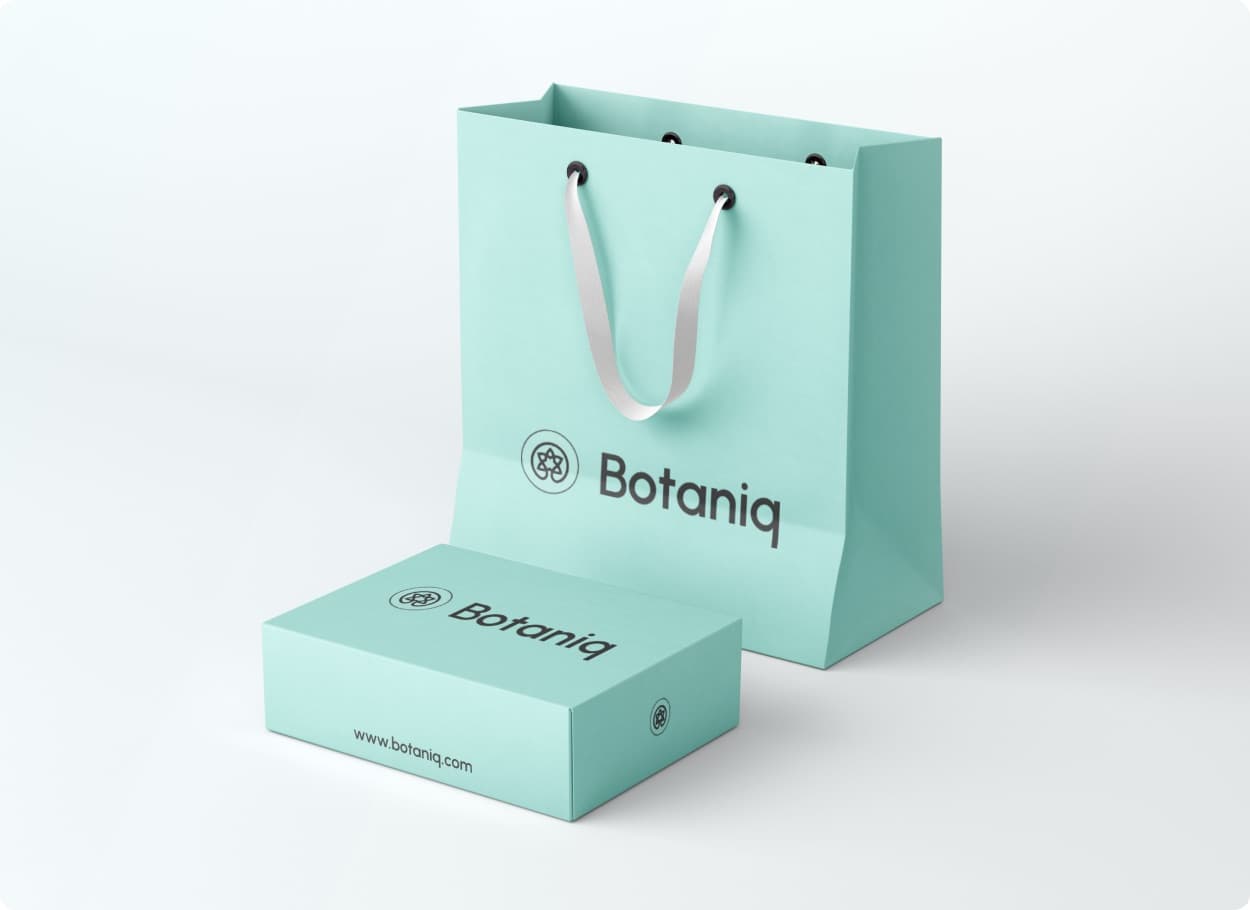 A mint green paper bag and box printed with the Botaniq mark and wordmark