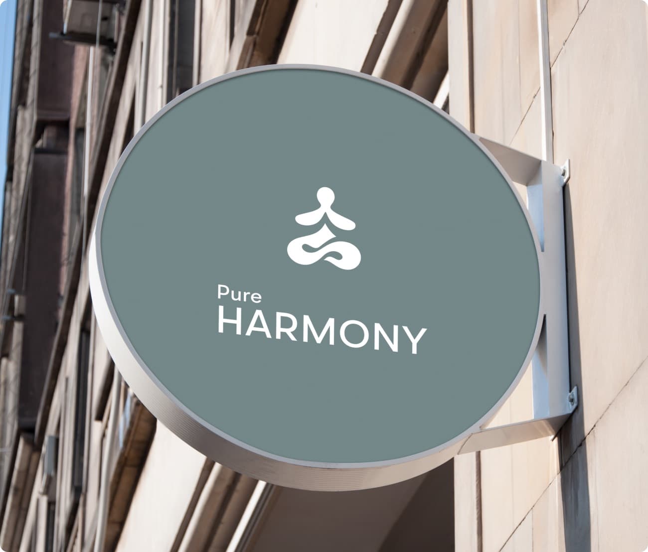 A round grey-green sign on a building wall, with the Pure Harmony seated-figure mark and wordmark in white